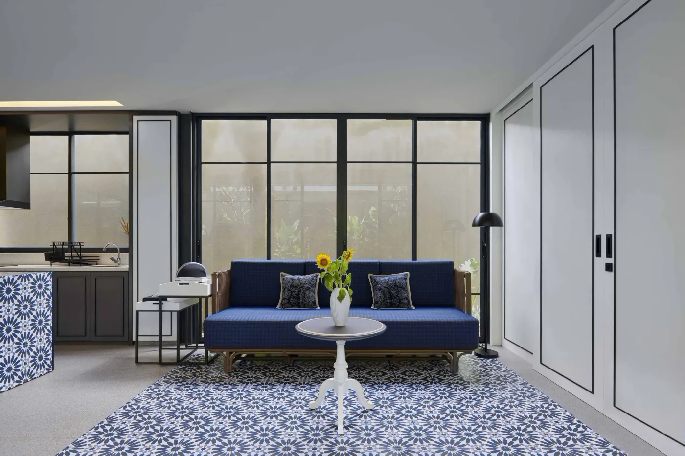 Modern open-plan room with blue mosaic tiled kitchen island, bar stools, blue sofa, bed, and large windows overlooking tropical garden. - Bali Villas
