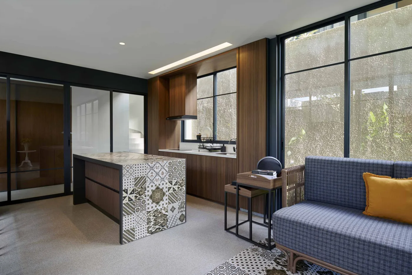 Modern open-plan room with blue mosaic tiled kitchen island, bar stools, blue sofa, bed, and large windows overlooking tropical garden. - Bali Villas