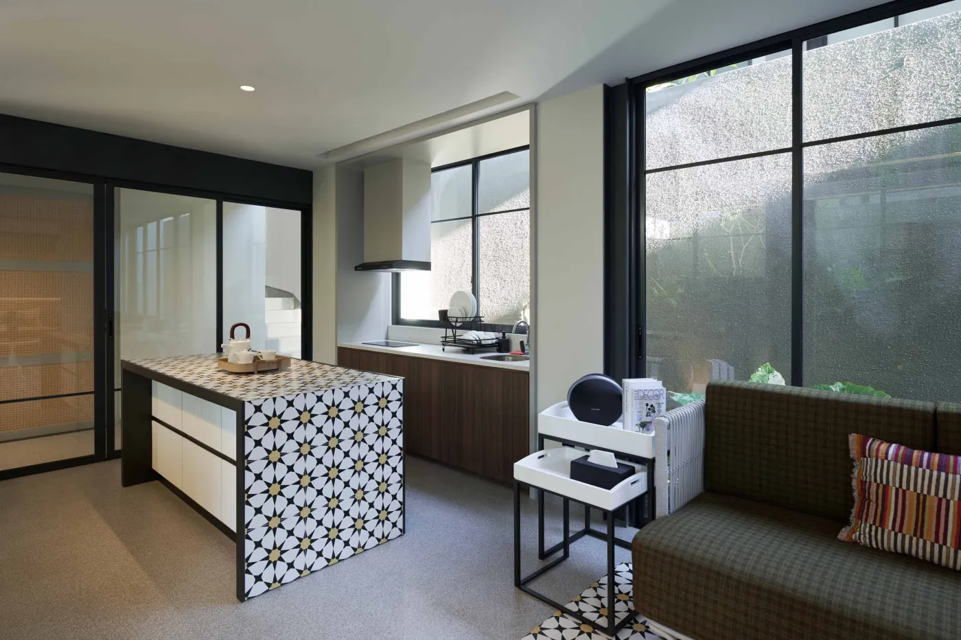 Modern open-plan room with blue mosaic tiled kitchen island, bar stools, blue sofa, bed, and large windows overlooking tropical garden. - Bali Villas