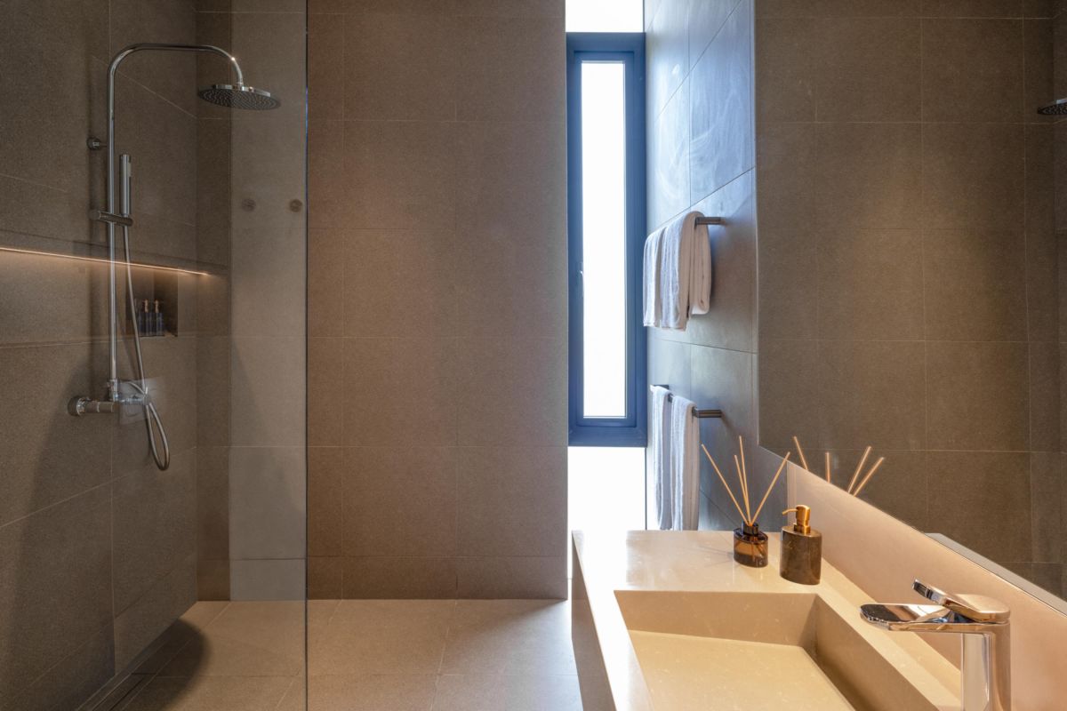 Modern luxury bathroom with freestanding white bathtub, gray stone walls, glass shower, and minimalist vanity. - Bali Villas