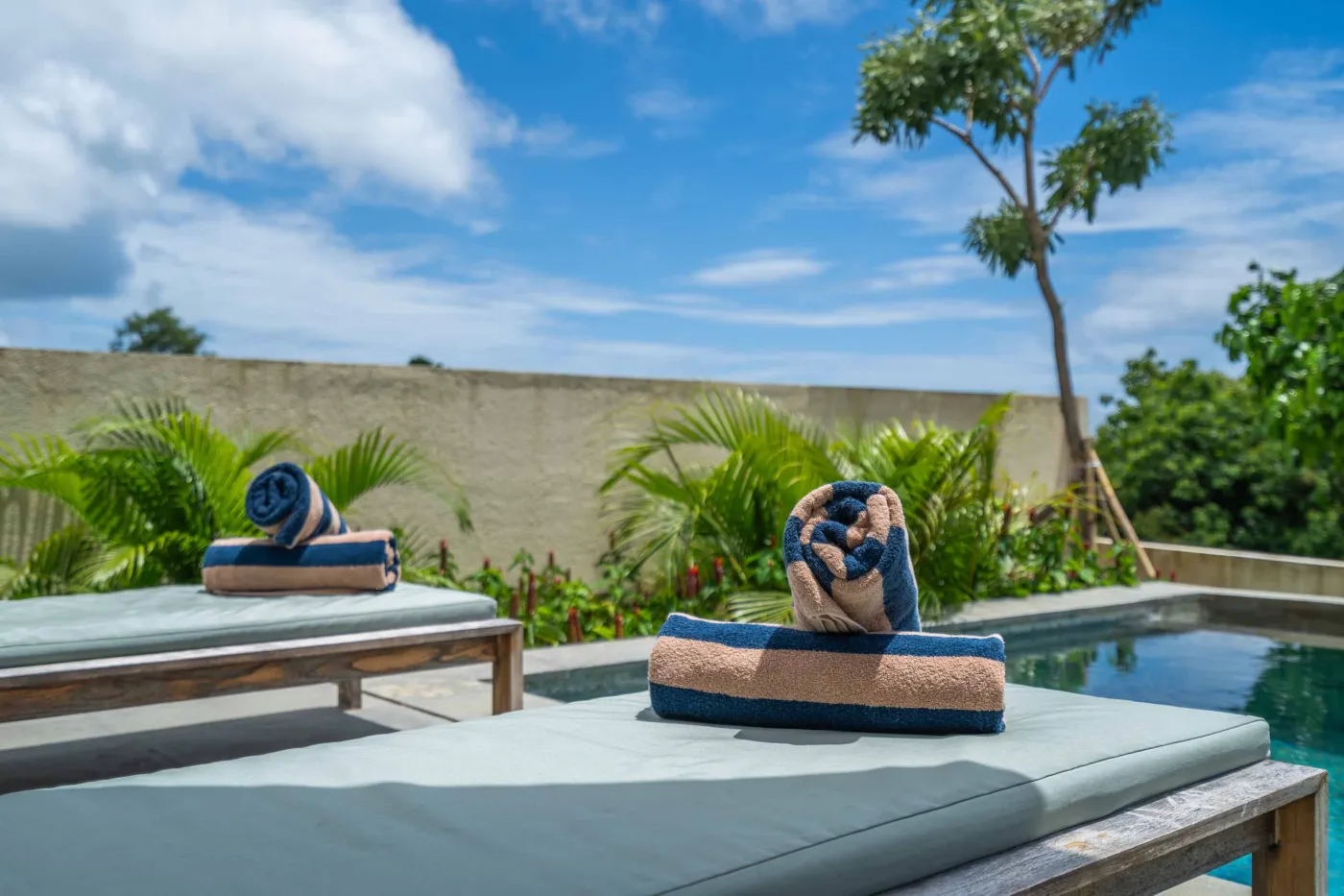 Blue and white striped towels rolled on a teal poolside lounger at a tropical resort villa. - Bali Villas