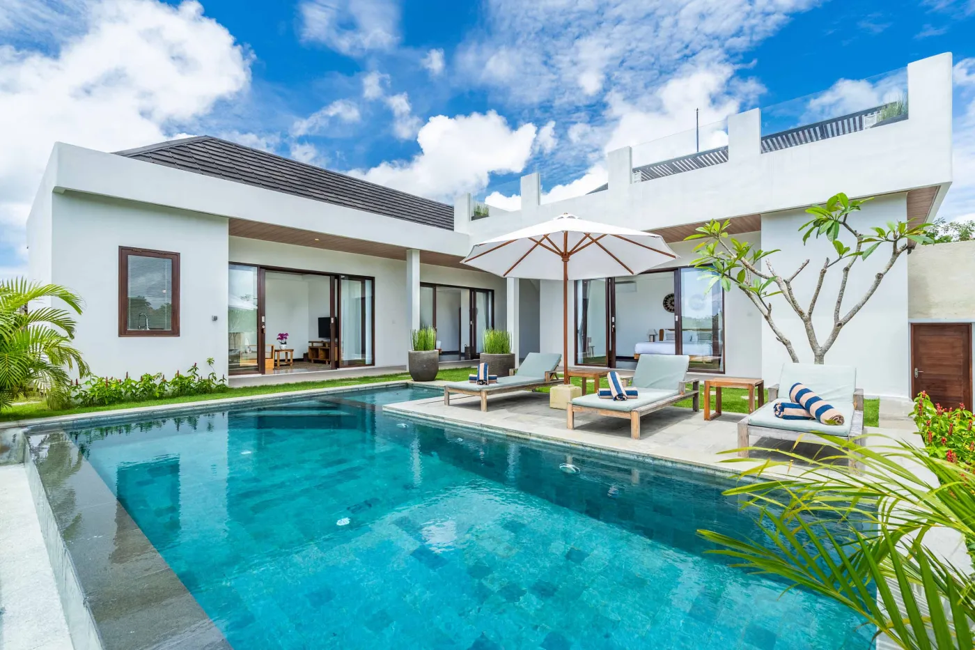 Blue and white striped towels rolled on a teal poolside lounger at a tropical resort villa. - Bali Villas