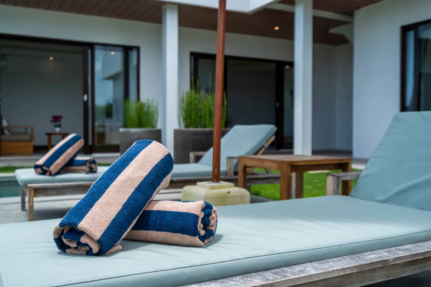Blue and white striped towels rolled on a teal poolside lounger at a tropical resort villa. - Bali Villas