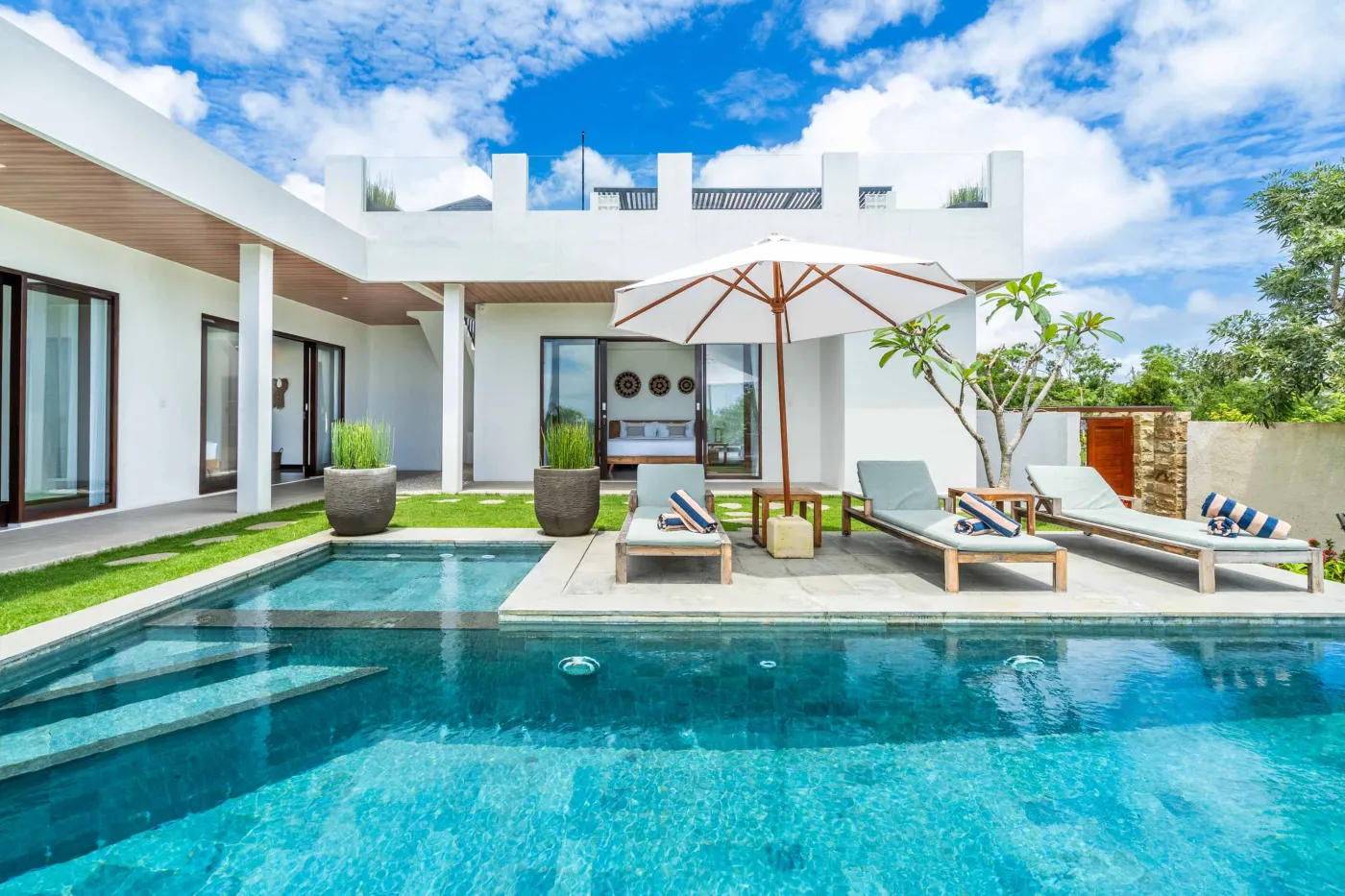 Blue and white striped towels rolled on a teal poolside lounger at a tropical resort villa. - Bali Villas