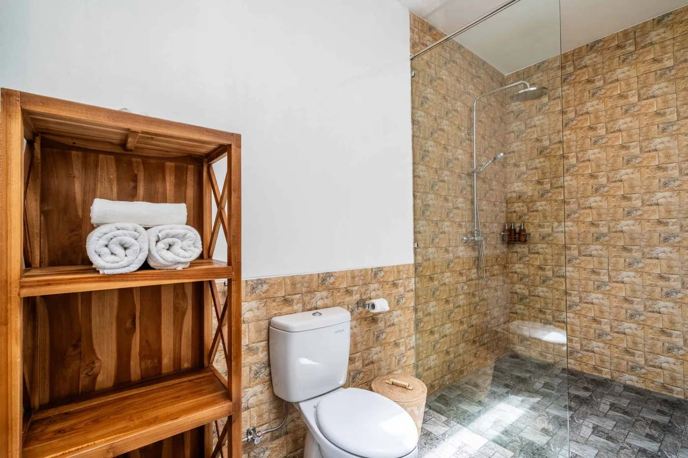 Modern tropical bathroom featuring brick-tiled shower, wooden vanity sink, toilet, and woven accents. - Bali Villas