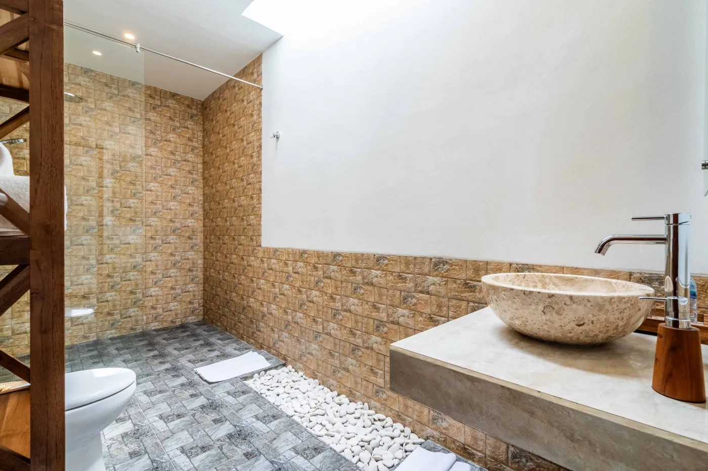 Modern tropical bathroom featuring brick-tiled shower, wooden vanity sink, toilet, and woven accents. - Bali Villas