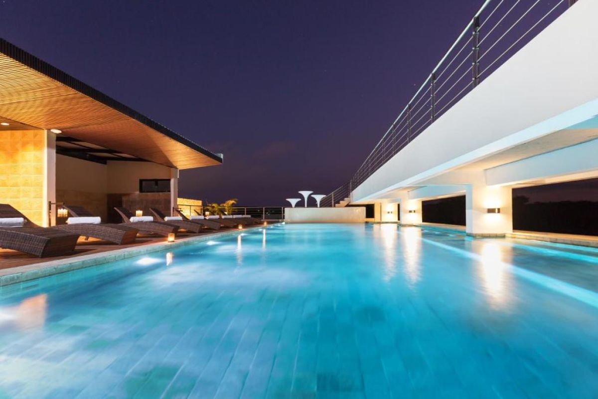 Twilight infinity pool with glowing blue water, lounge chairs on wooden deck, and modern resort architecture at dusk. - Bali Villas