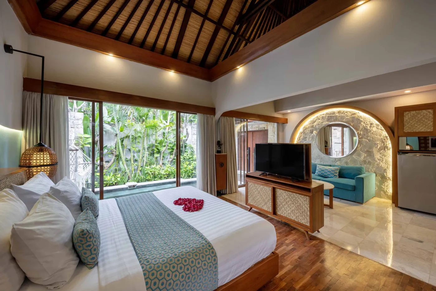 Cozy Balinese villa interior with thatched ceiling, turquoise sofa, wooden kitchenette, arched stone doorway, and round mirrors. - Bali Villas
