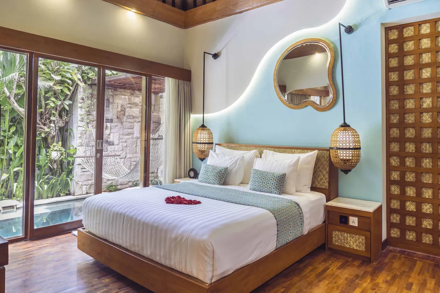 Cozy Balinese villa interior with thatched ceiling, turquoise sofa, wooden kitchenette, arched stone doorway, and round mirrors. - Bali Villas