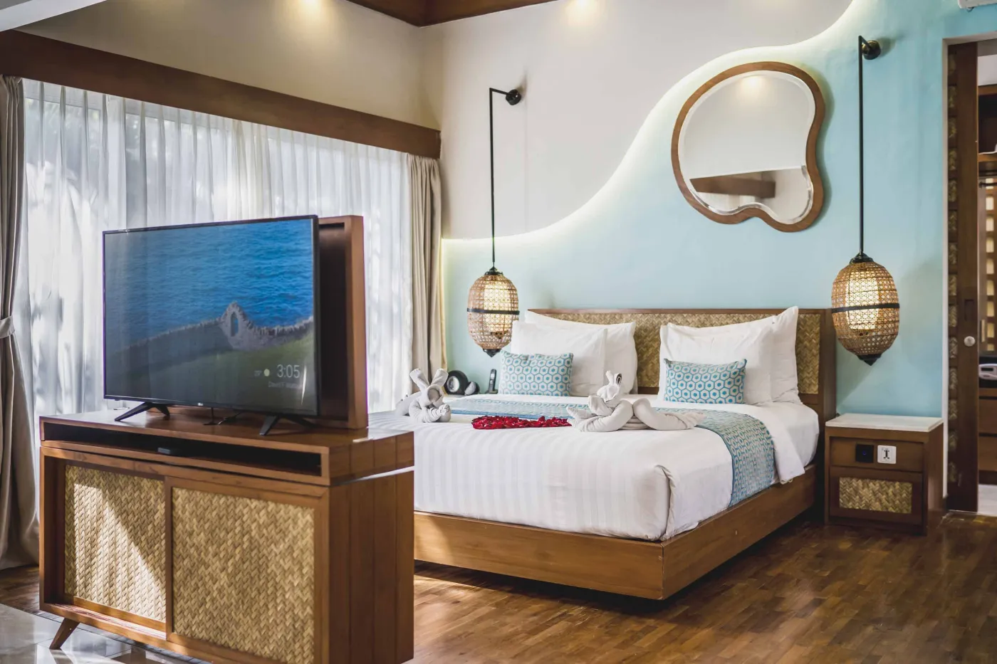 Cozy Balinese villa interior with thatched ceiling, turquoise sofa, wooden kitchenette, arched stone doorway, and round mirrors. - Bali Villas