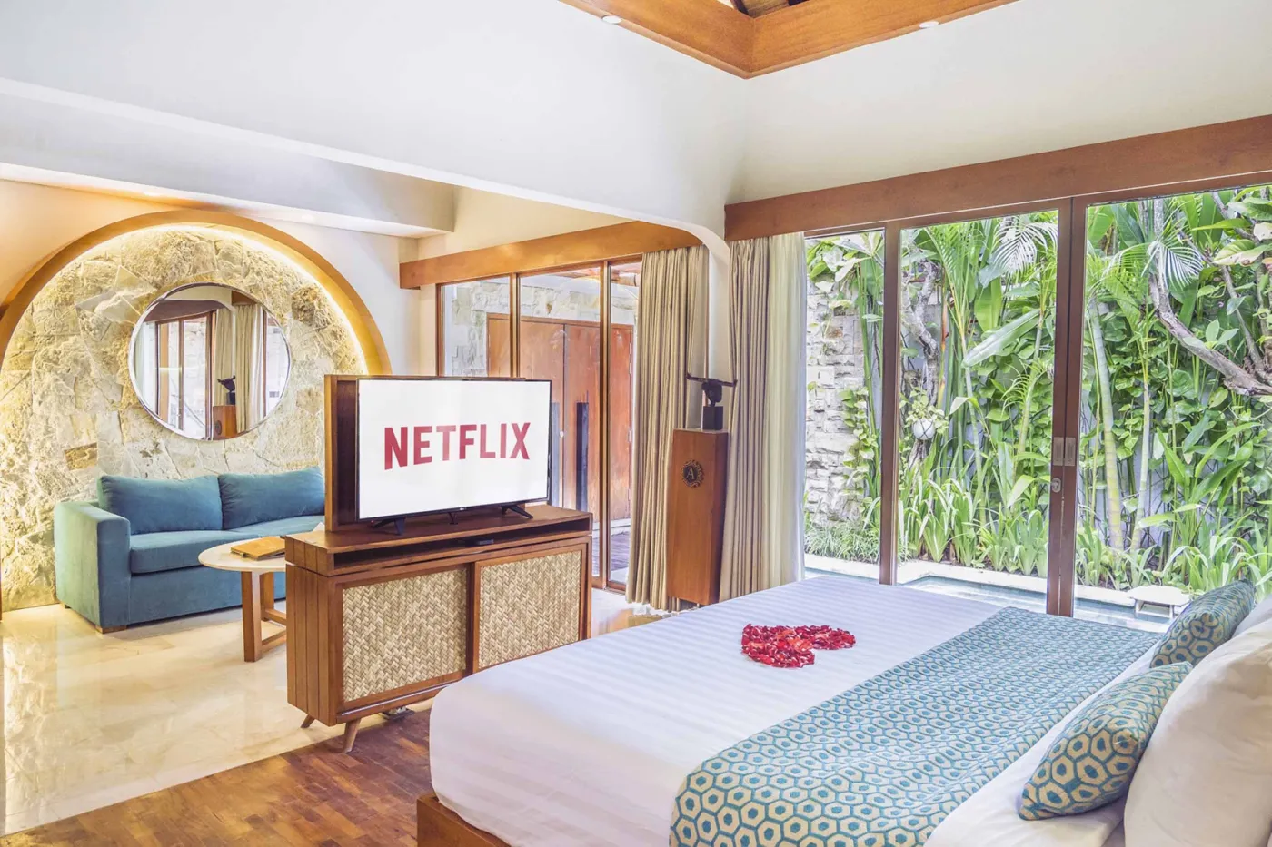 Cozy Balinese villa interior with thatched ceiling, turquoise sofa, wooden kitchenette, arched stone doorway, and round mirrors. - Bali Villas