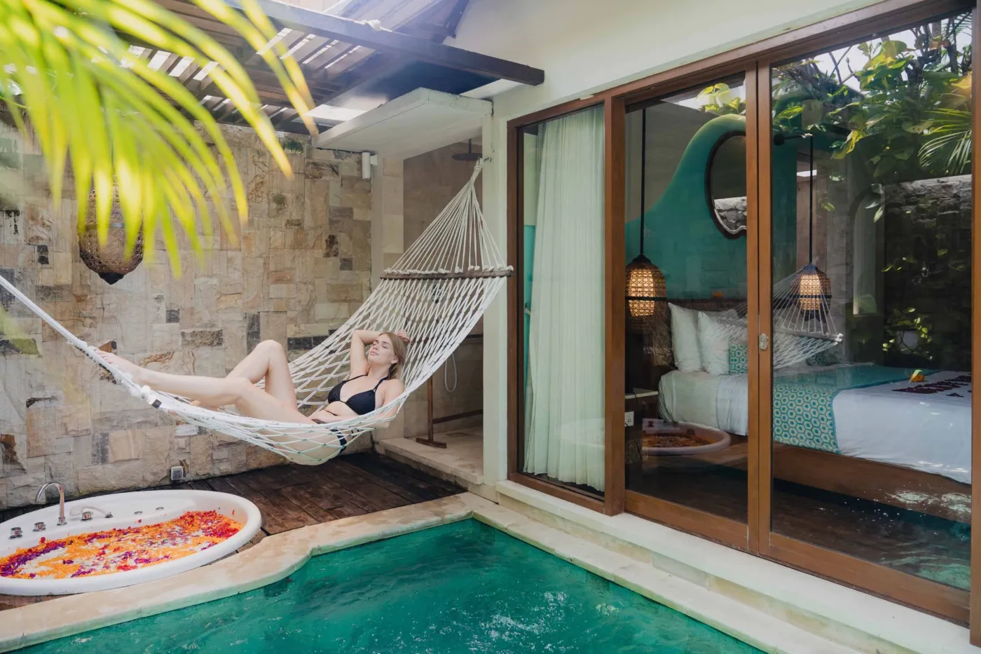 Cozy Balinese villa interior with thatched ceiling, turquoise sofa, wooden kitchenette, arched stone doorway, and round mirrors. - Bali Villas