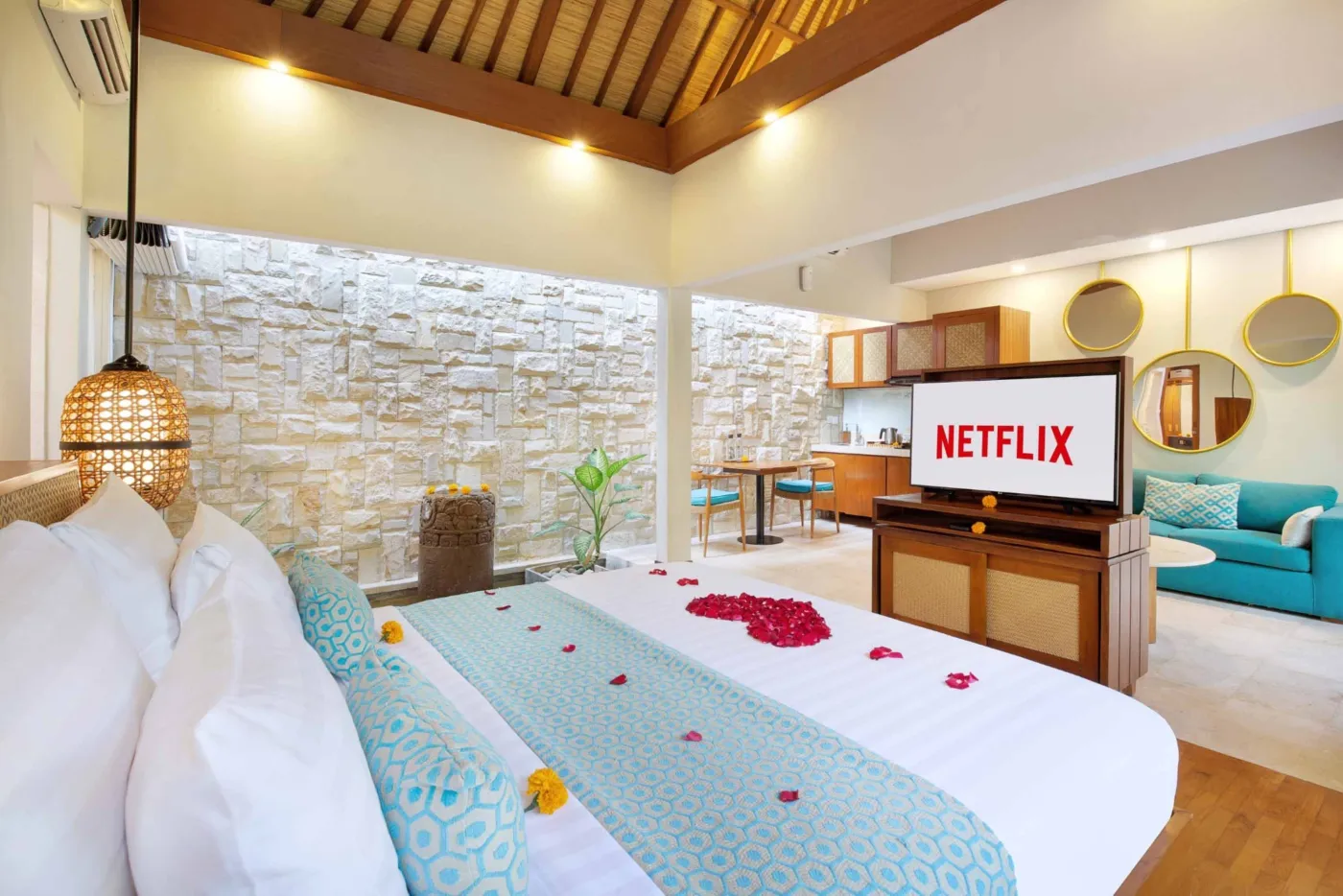 Cozy Balinese villa interior with thatched ceiling, turquoise sofa, wooden kitchenette, arched stone doorway, and round mirrors. - Bali Villas