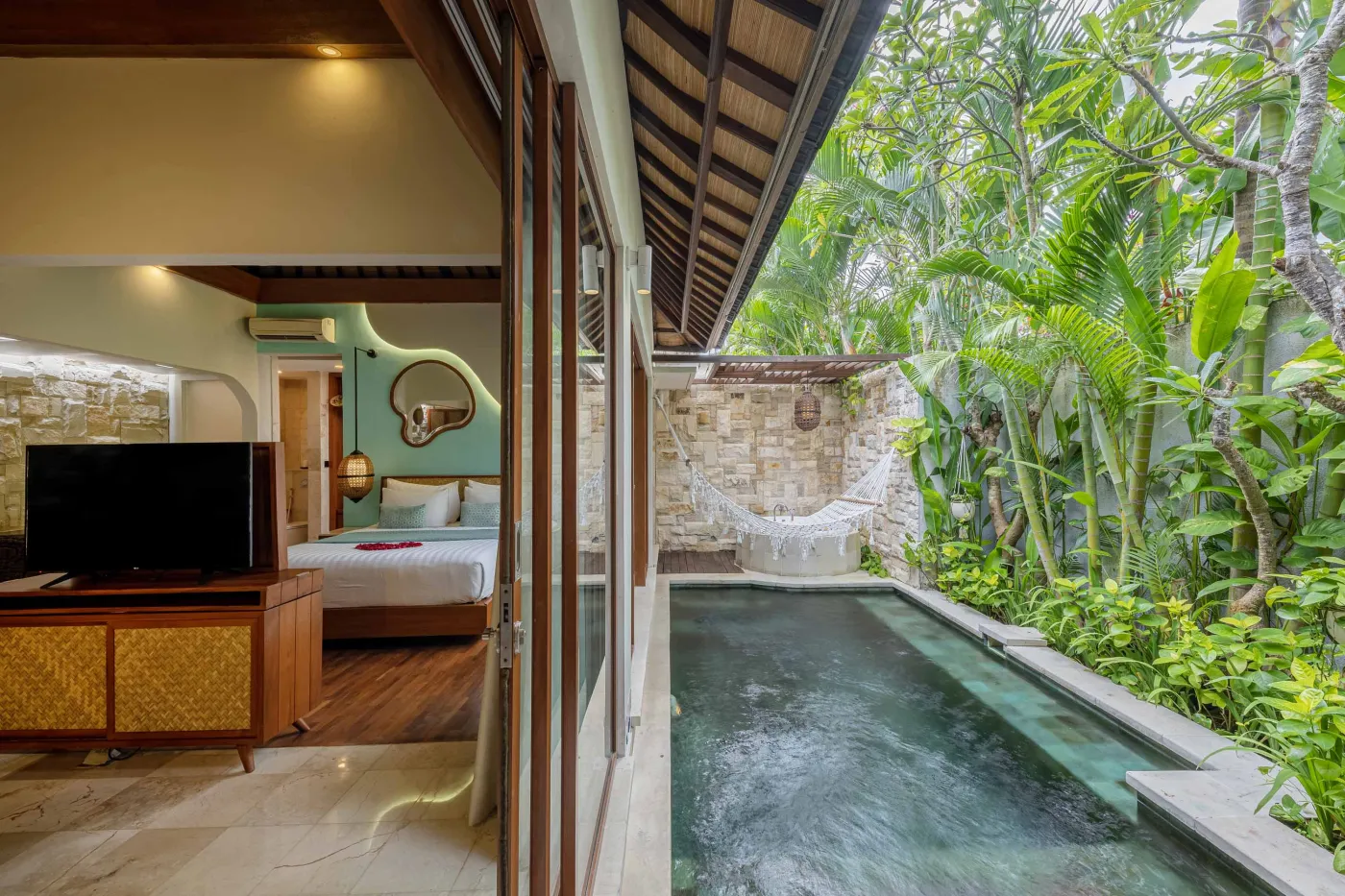 Cozy Balinese villa interior with thatched ceiling, turquoise sofa, wooden kitchenette, arched stone doorway, and round mirrors. - Bali Villas