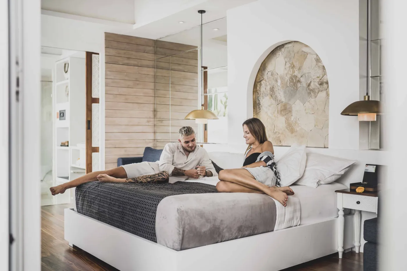 Modern Balinese-style reception lobby with wooden desk, blue armchairs, tropical plants, and glass doors to outdoor greenery. - Bali Villas