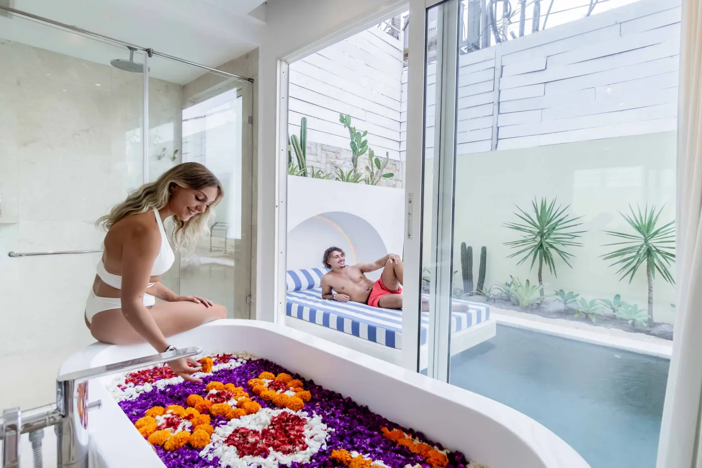 Modern Balinese-style reception lobby with wooden desk, blue armchairs, tropical plants, and glass doors to outdoor greenery. - Bali Villas