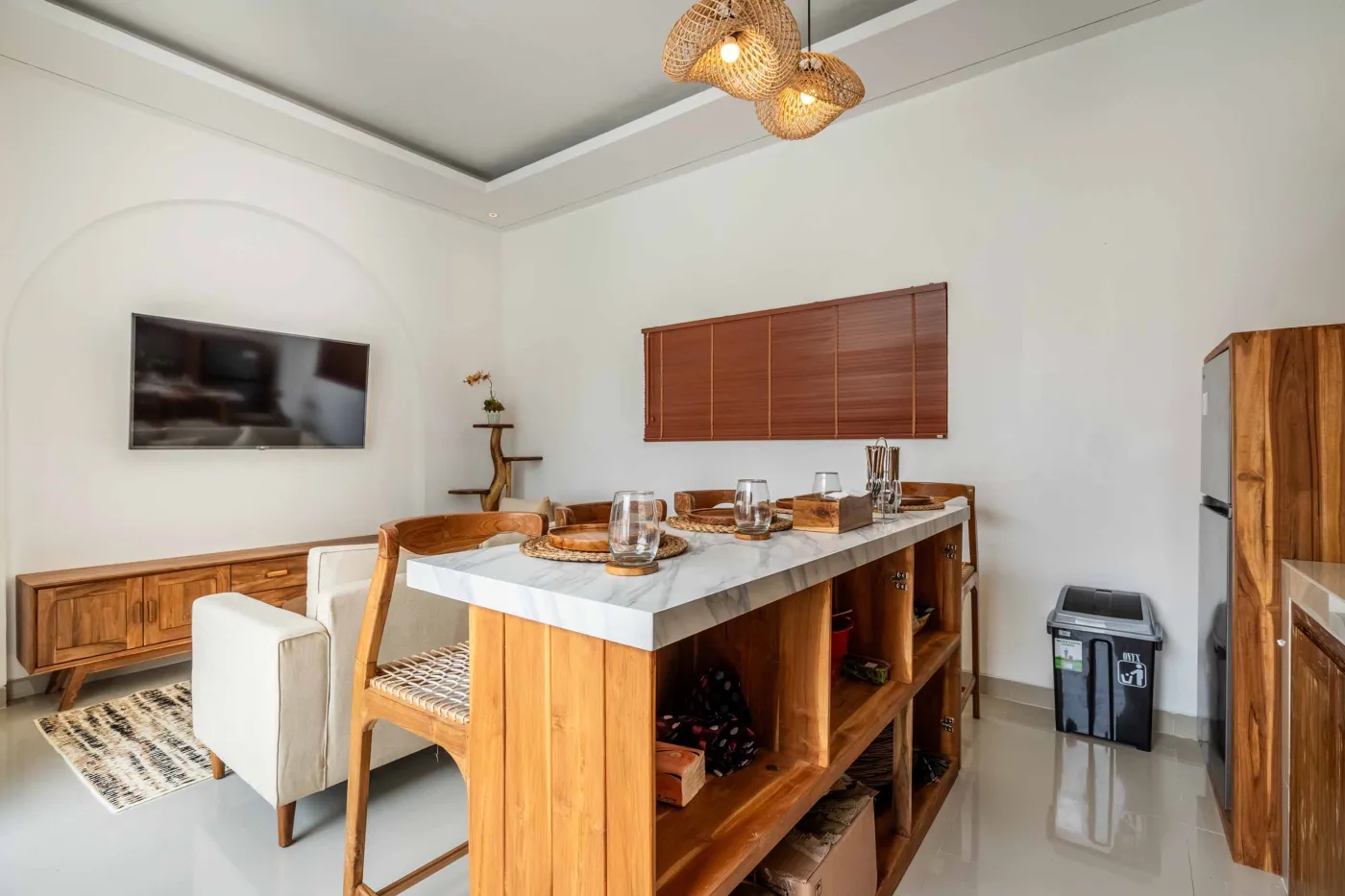 Modern compact bathroom with white tiles, glass shower enclosure, wooden shelves, white toilet, sink, and ornate oval mirror. - Bali Villas