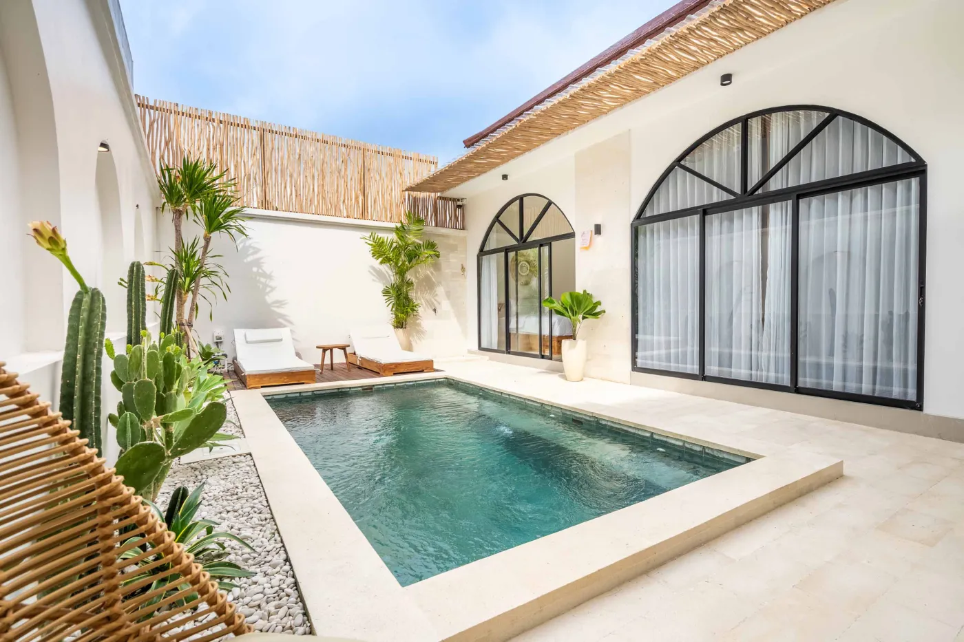 Modern compact bathroom with white tiles, glass shower enclosure, wooden shelves, white toilet, sink, and ornate oval mirror. - Bali Villas