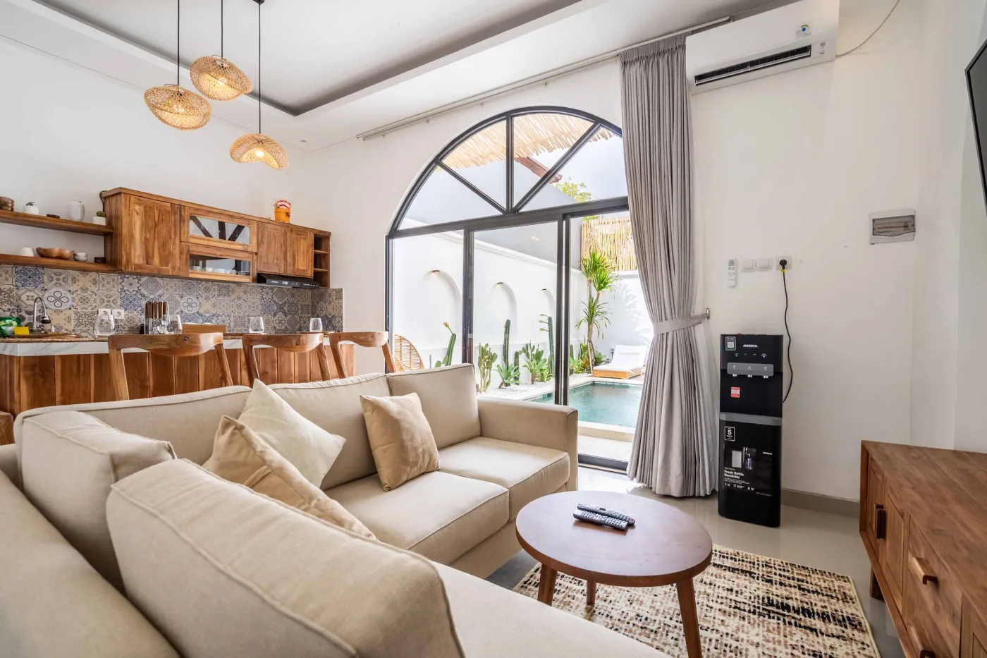 Modern compact bathroom with white tiles, glass shower enclosure, wooden shelves, white toilet, sink, and ornate oval mirror. - Bali Villas