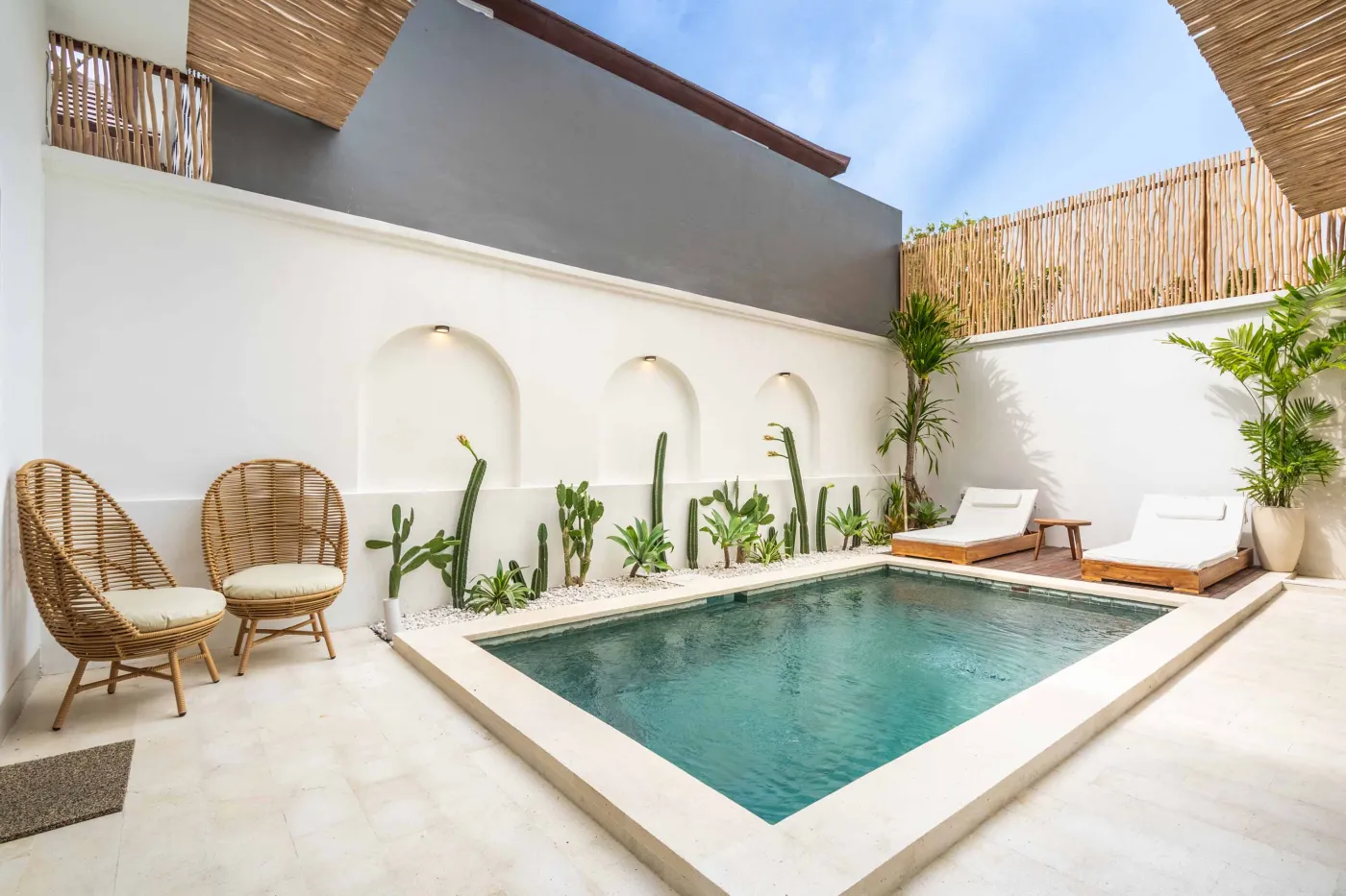 Modern compact bathroom with white tiles, glass shower enclosure, wooden shelves, white toilet, sink, and ornate oval mirror. - Bali Villas