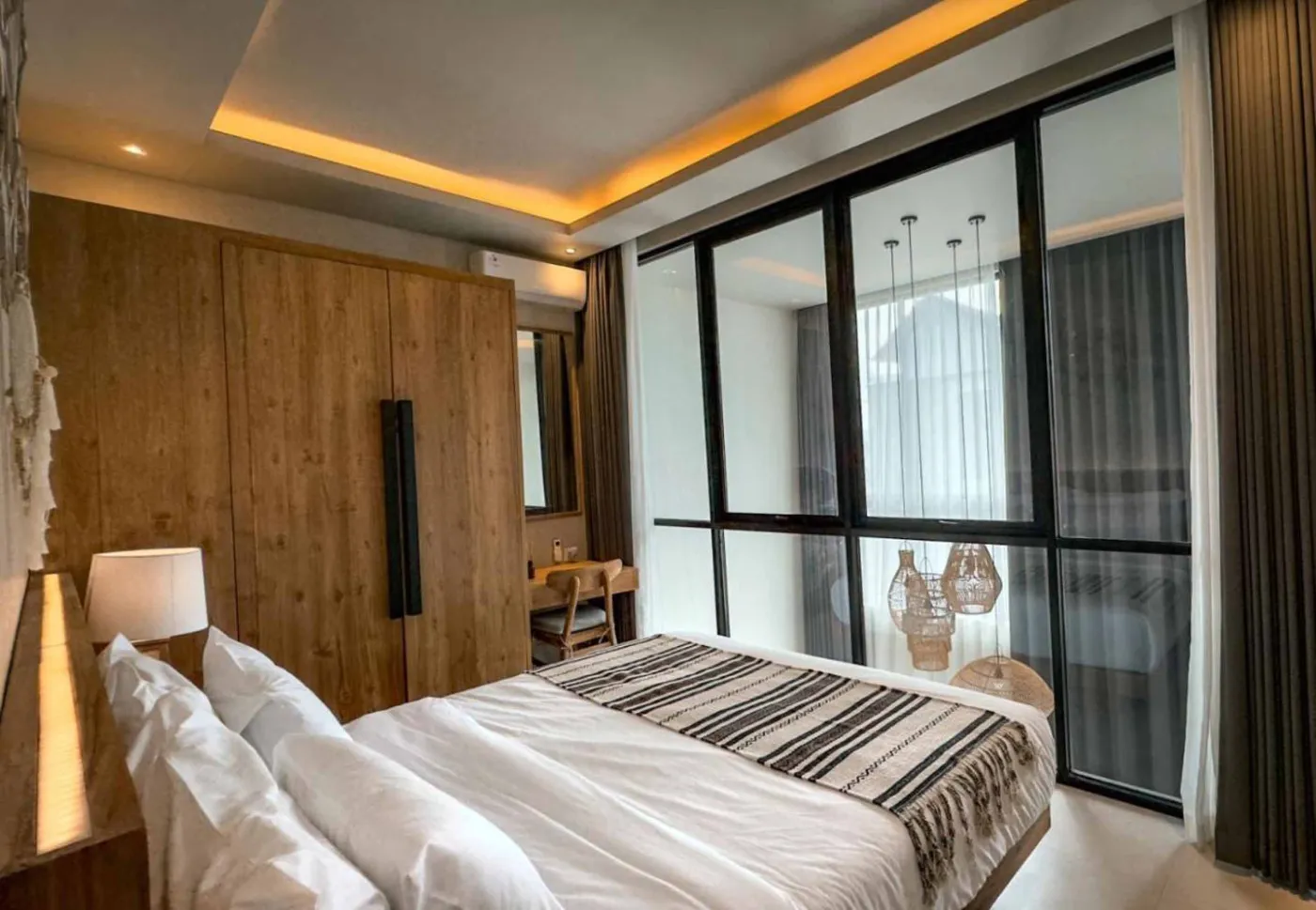 Modern Balinese villa interior: open kitchen with wooden cabinets, granite island, tiled backsplash, and dining table with pink orchids, overlooking a green balcony. - Bali Villas