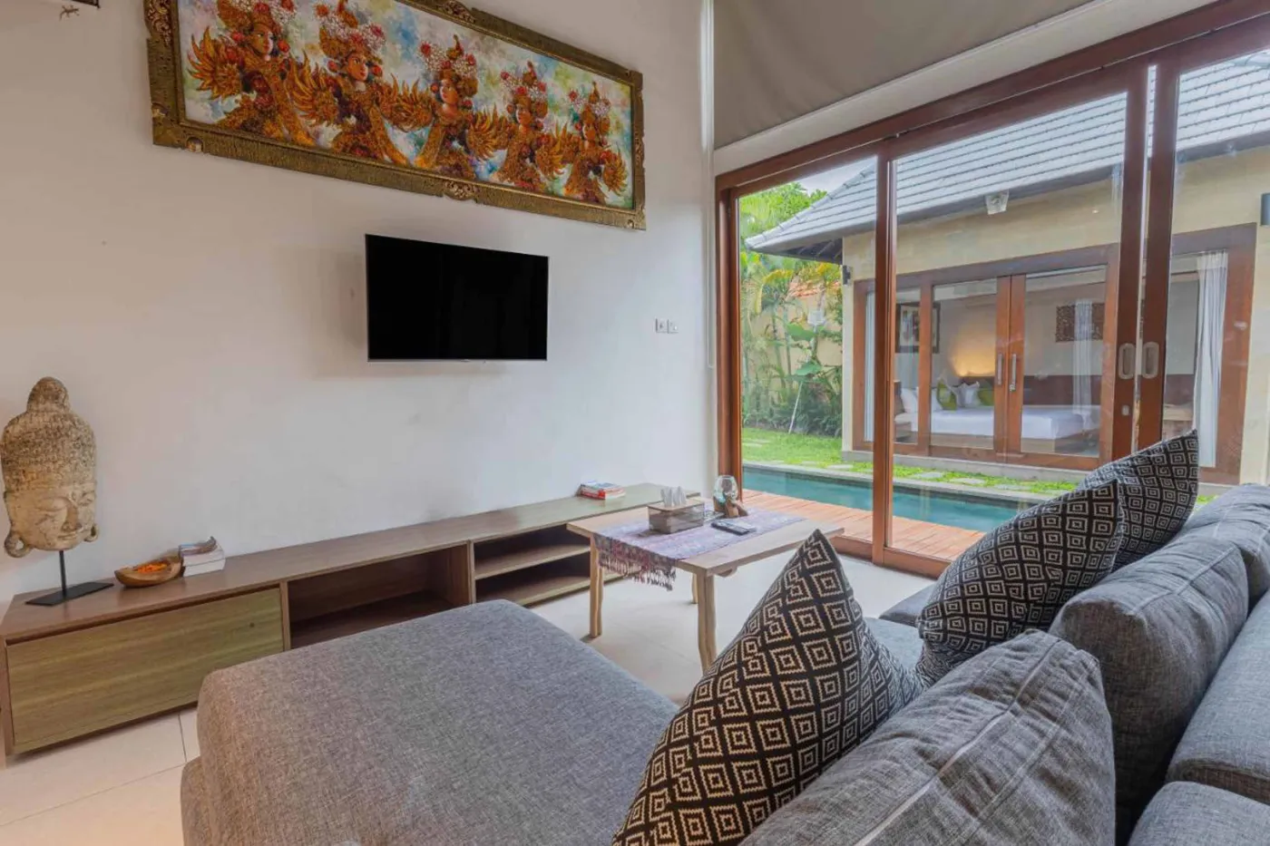 Modern Balinese villa interior: open kitchen with wooden cabinets, granite island, tiled backsplash, and dining table with pink orchids, overlooking a green balcony. - Bali Villas
