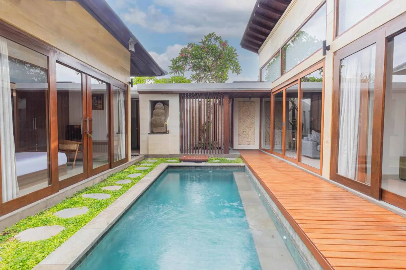 Modern Balinese villa interior: open kitchen with wooden cabinets, granite island, tiled backsplash, and dining table with pink orchids, overlooking a green balcony. - Bali Villas