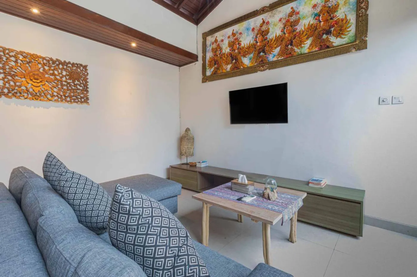 Modern Balinese villa interior: open kitchen with wooden cabinets, granite island, tiled backsplash, and dining table with pink orchids, overlooking a green balcony. - Bali Villas