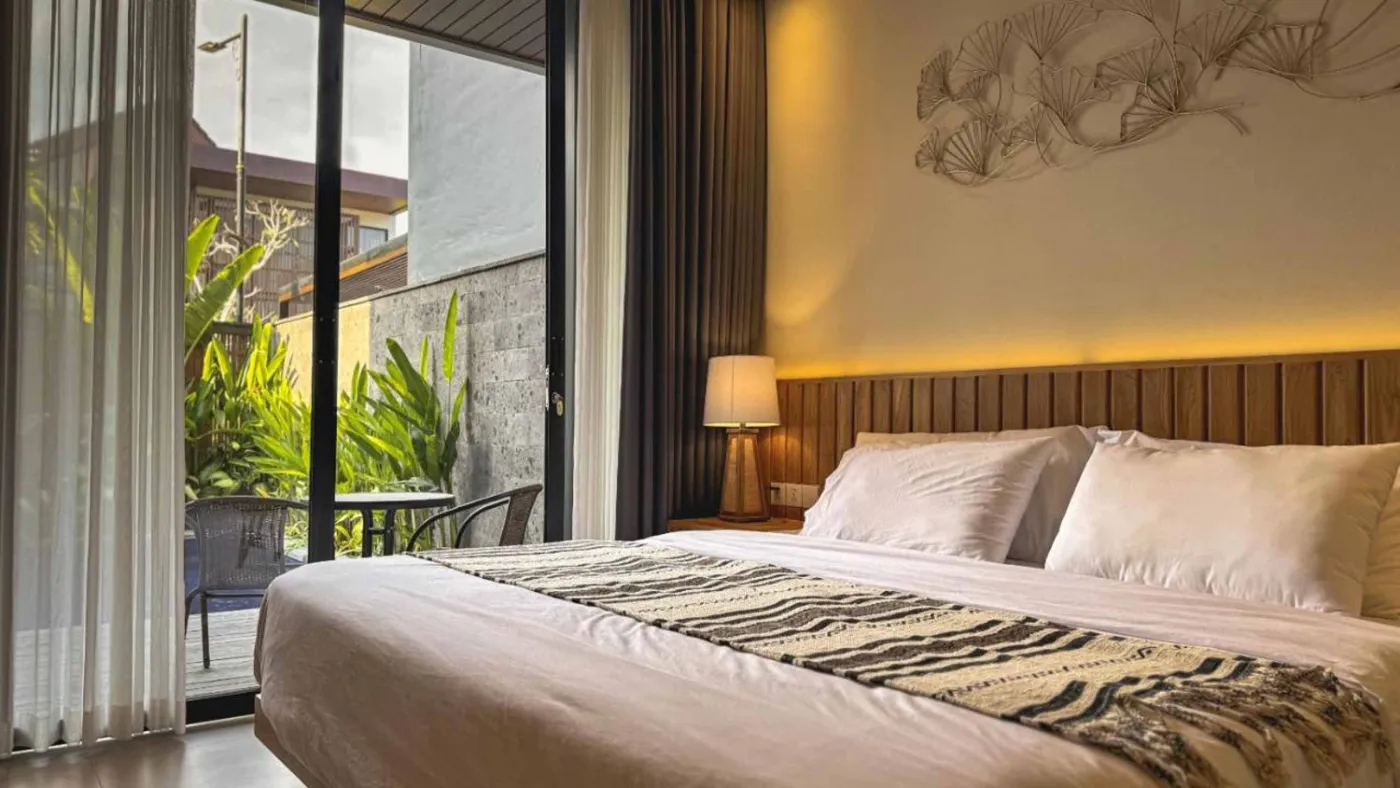 Modern Balinese villa interior: open kitchen with wooden cabinets, granite island, tiled backsplash, and dining table with pink orchids, overlooking a green balcony. - Bali Villas