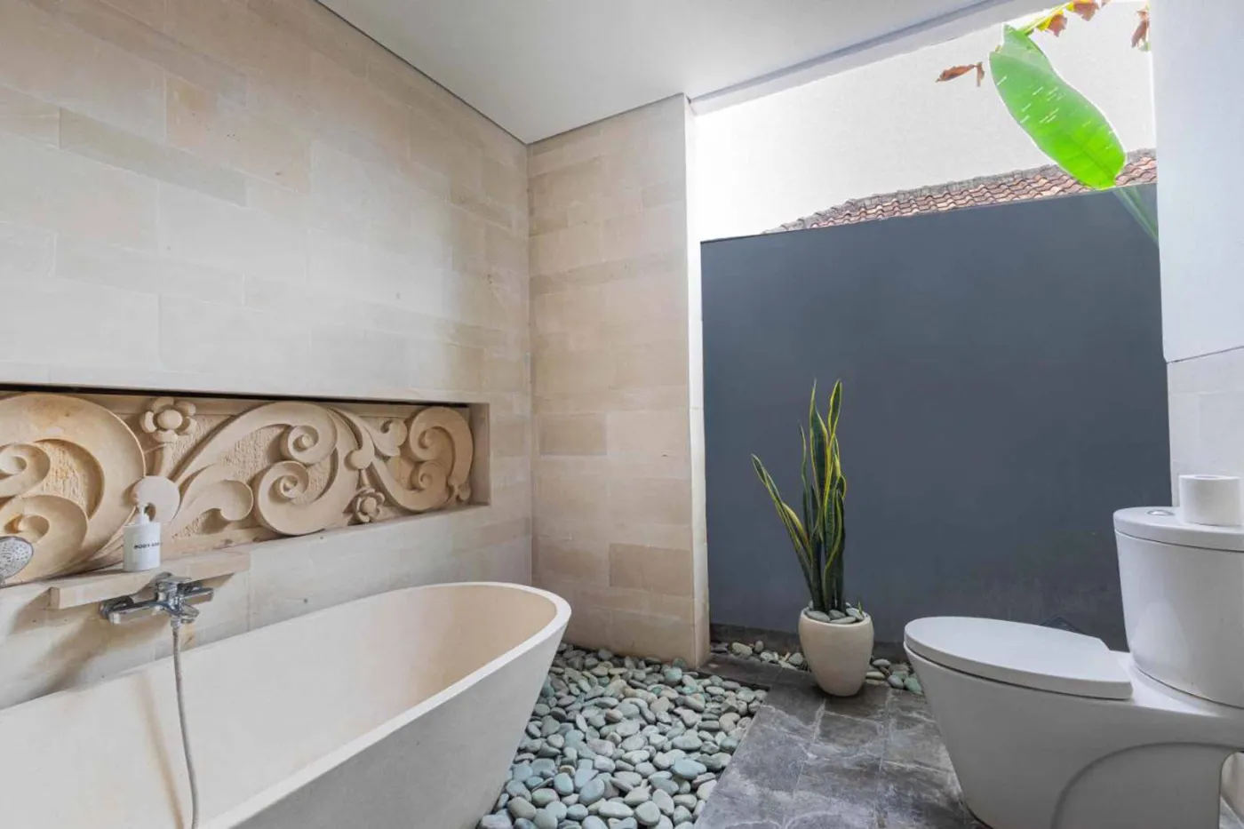 Modern Balinese villa interior: open kitchen with wooden cabinets, granite island, tiled backsplash, and dining table with pink orchids, overlooking a green balcony. - Bali Villas