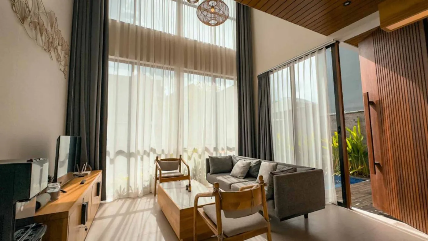 Modern Balinese villa interior: open kitchen with wooden cabinets, granite island, tiled backsplash, and dining table with pink orchids, overlooking a green balcony. - Bali Villas