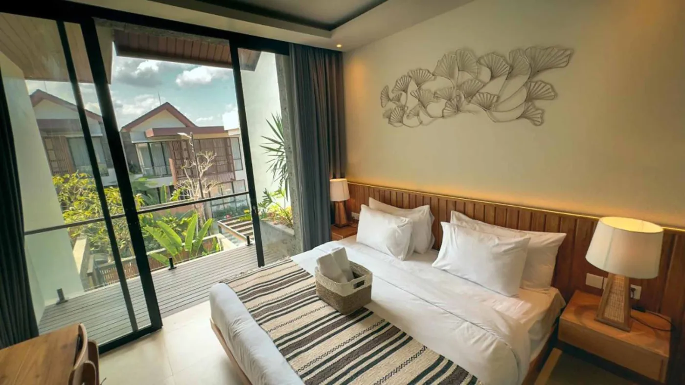 Modern Balinese villa interior: open kitchen with wooden cabinets, granite island, tiled backsplash, and dining table with pink orchids, overlooking a green balcony. - Bali Villas