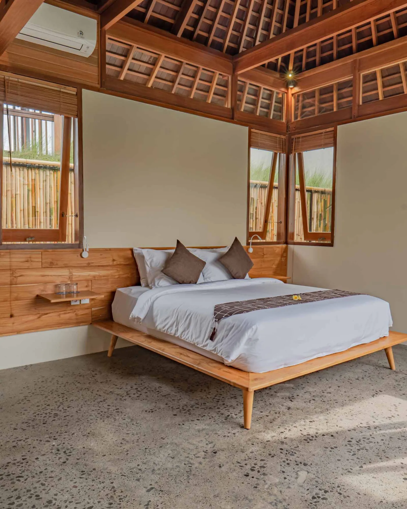Spacious wooden kitchen and dining area in a tropical Balinese-style villa, featuring a set table with plates, glasses, vibrant floral centerpiece, and lush garden view through open sliding doors. - Bali Villas