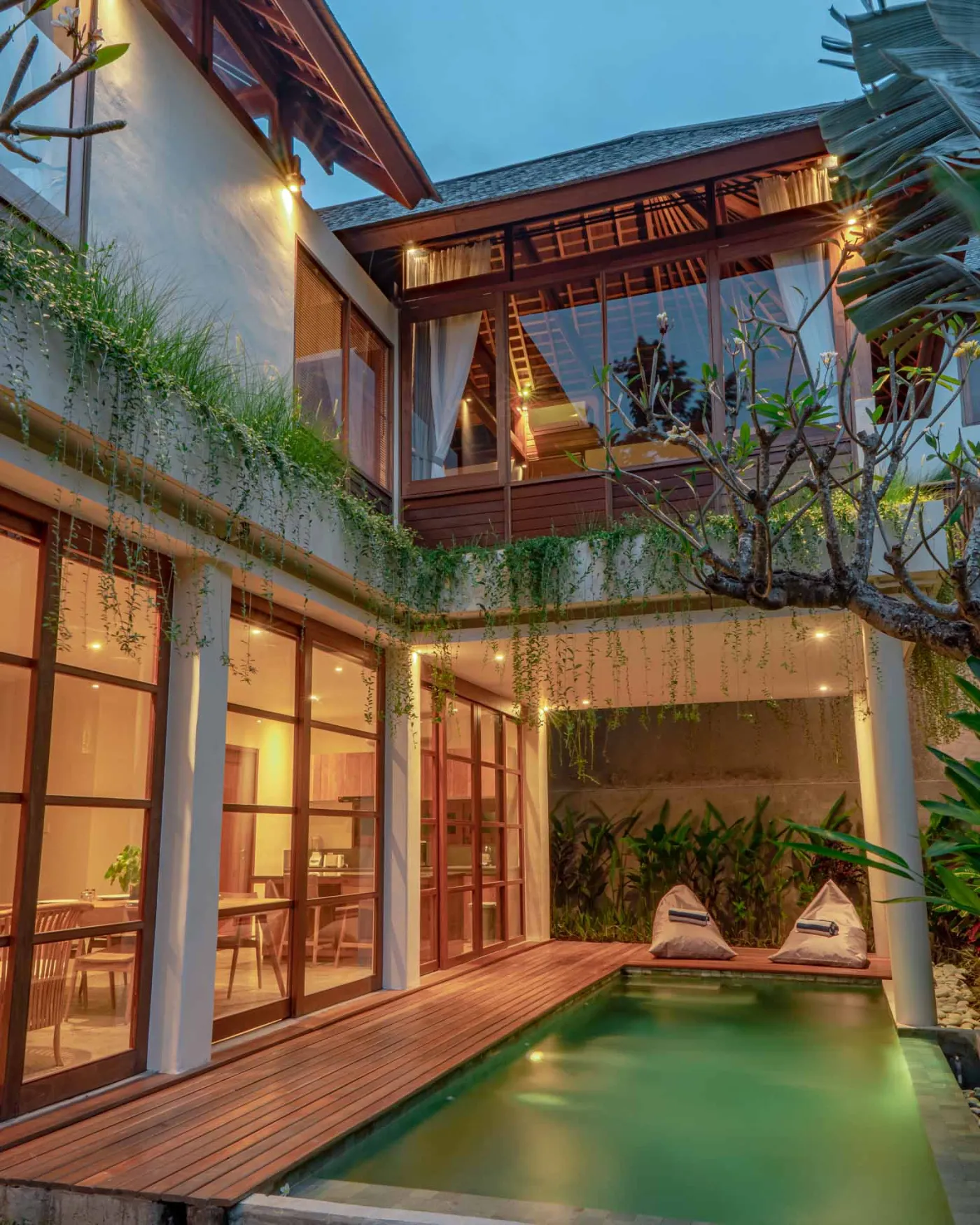 Spacious wooden kitchen and dining area in a tropical Balinese-style villa, featuring a set table with plates, glasses, vibrant floral centerpiece, and lush garden view through open sliding doors. - Bali Villas