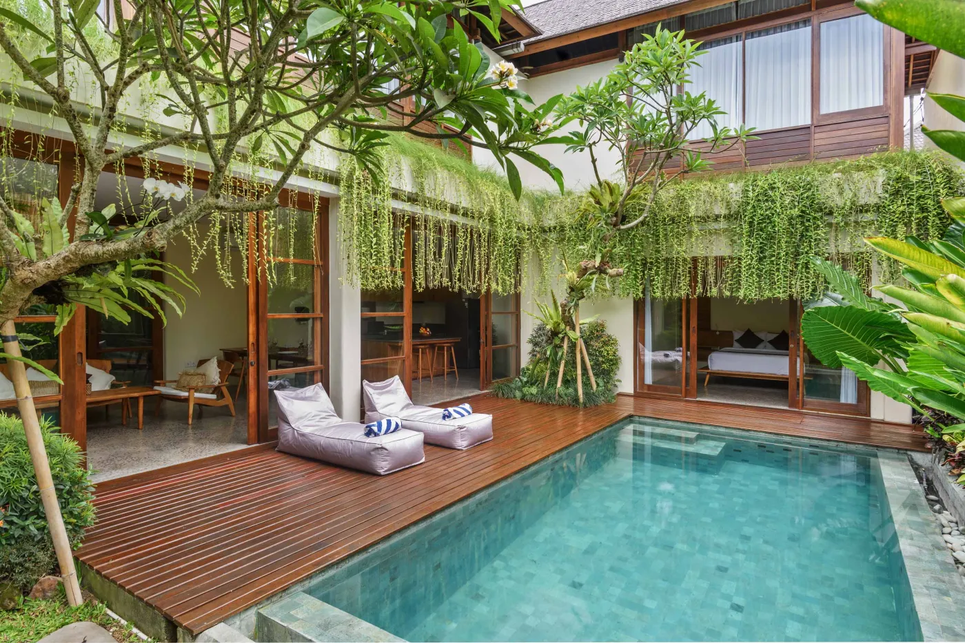 Luxurious Balinese villa poolside with turquoise infinity pool, cushioned loungers, and lush tropical greenery. - Bali Villas