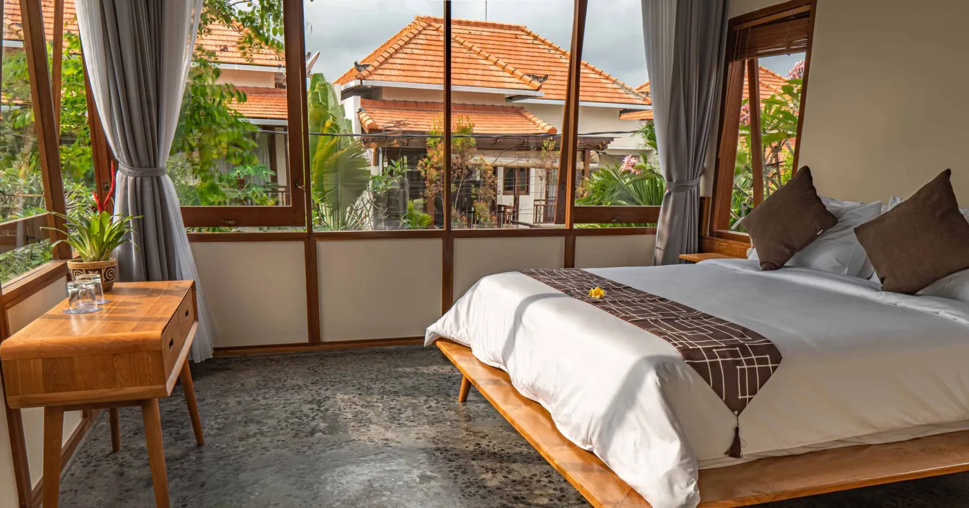 Spacious wooden kitchen and dining area in a tropical Balinese-style villa, featuring a set table with plates, glasses, vibrant floral centerpiece, and lush garden view through open sliding doors. - Bali Villas