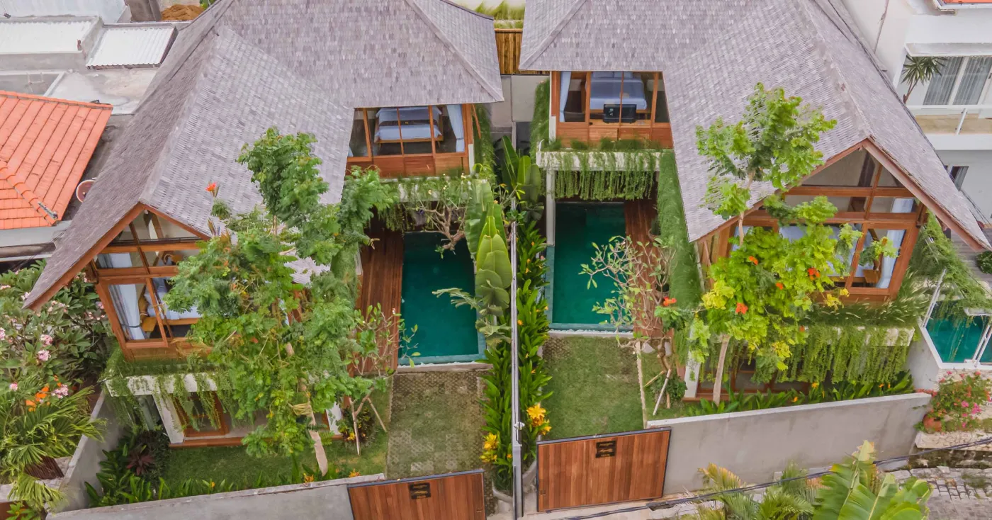 Spacious wooden kitchen and dining area in a tropical Balinese-style villa, featuring a set table with plates, glasses, vibrant floral centerpiece, and lush garden view through open sliding doors. - Bali Villas