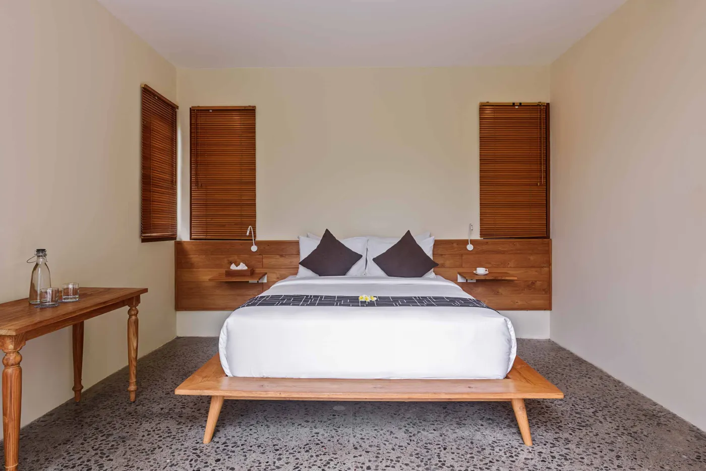 Modern open-plan living and dining area in a tropical villa with wooden furniture, large sliding doors to poolside garden, and lush greenery. - Bali Villas