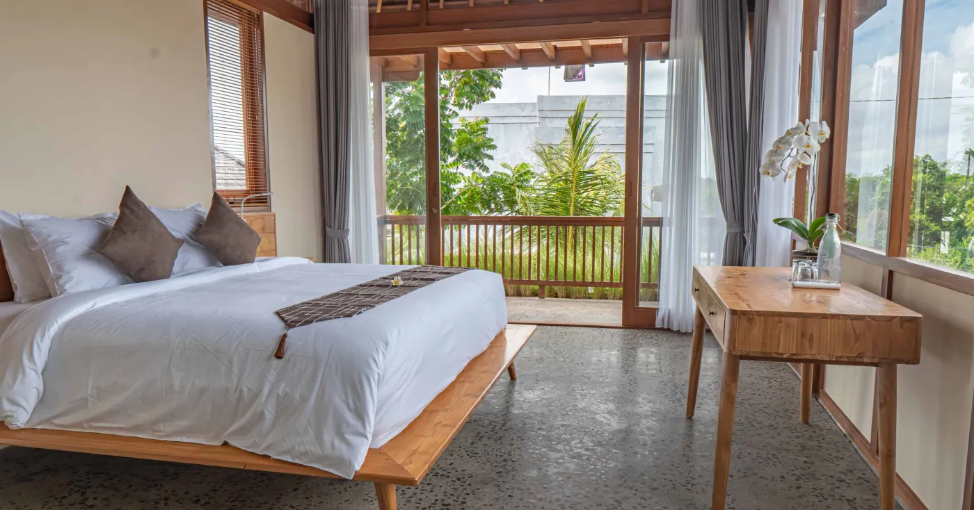 Modern tropical living room with wooden sofa, armchairs, low coffee table, potted orchid, wall-mounted TV, and open doors to lush garden. - Bali Villas