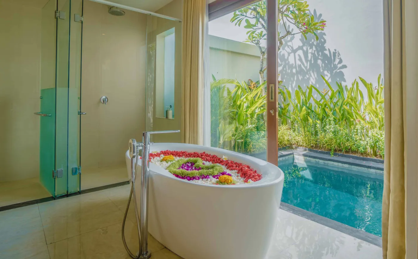 Bright modern Bali villa kitchen and dining area with wooden cabinets, rattan table topped with tropical fruits, ceiling fan, and sliding doors to lush garden. - Bali Villas