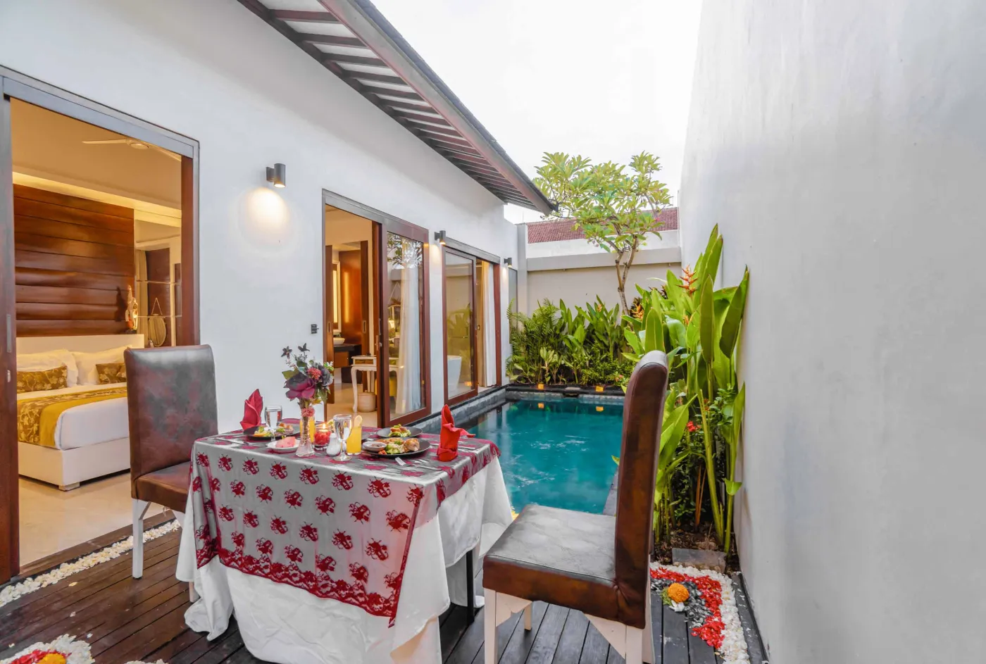 Bright modern Bali villa kitchen and dining area with wooden cabinets, rattan table topped with tropical fruits, ceiling fan, and sliding doors to lush garden. - Bali Villas