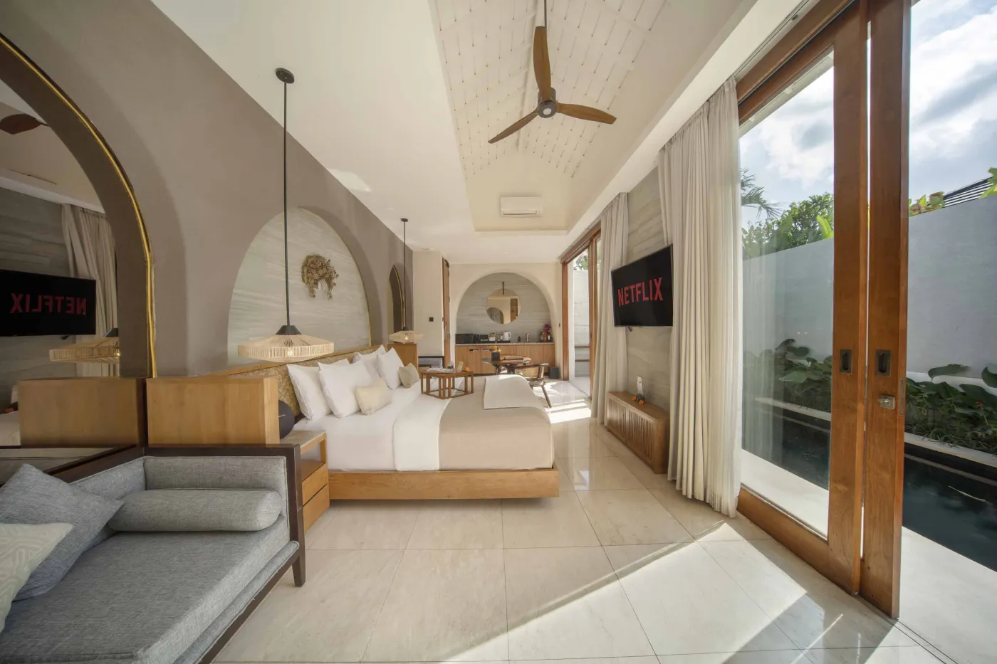 Spacious luxury tropical bedroom with king bed, wooden accents, ceiling fan, and poolside garden view through large windows. - Bali Villas