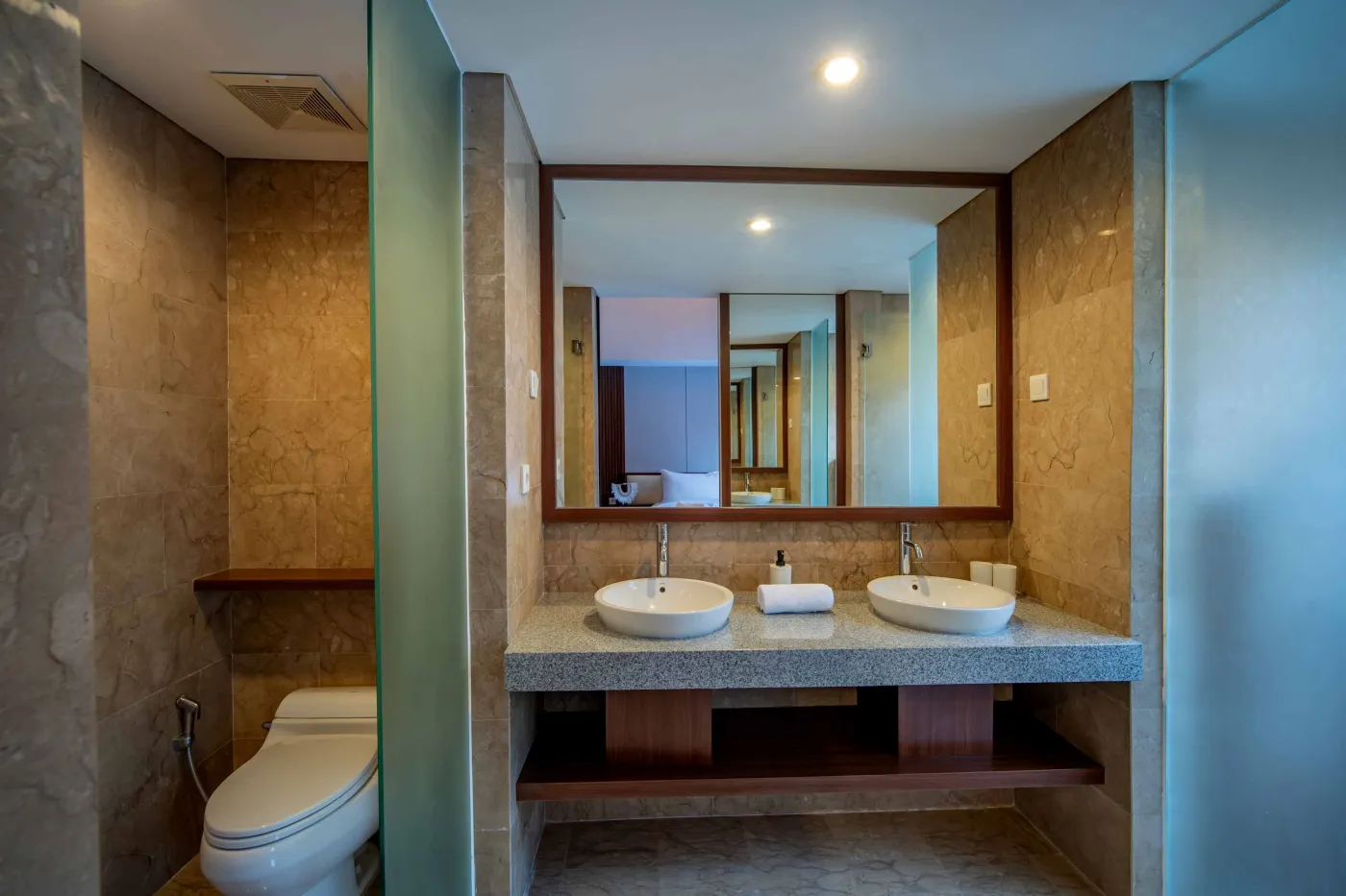 Modern hotel bathroom with double vanity sinks, large framed mirror, and frosted glass shower enclosure. - Bali Villas