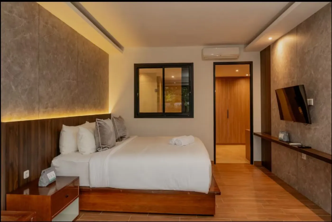 Modern wooden kitchen interior with white countertops, gas stove, sink, LED-lit backsplash, open shelves, and a small dining table with chairs. - Bali Villas