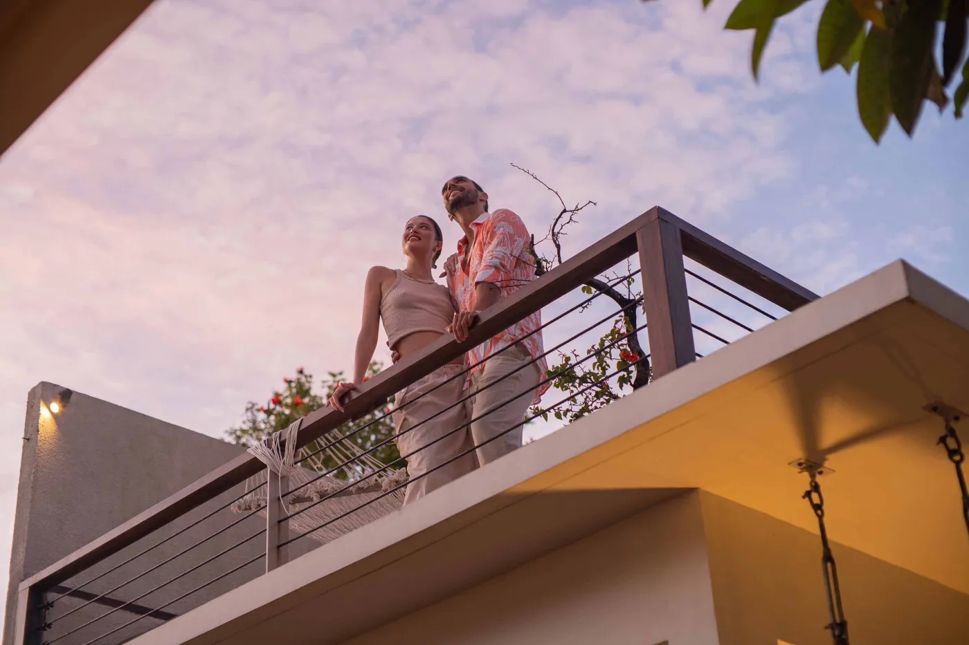 Romantic couple embracing on a modern balcony at sunset, surrounded by tropical plants. - Bali Villas
