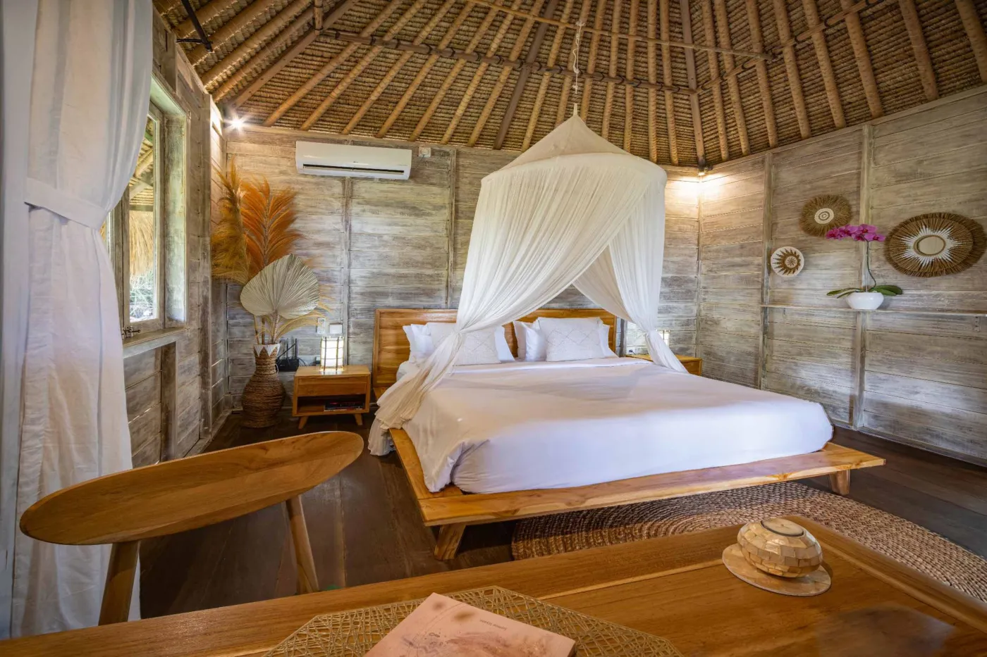 Luxurious Balinese veranda at sunset overlooking ocean and infinity pool, with wooden furniture, tropical plants, and cushioned seating. - Bali Villas