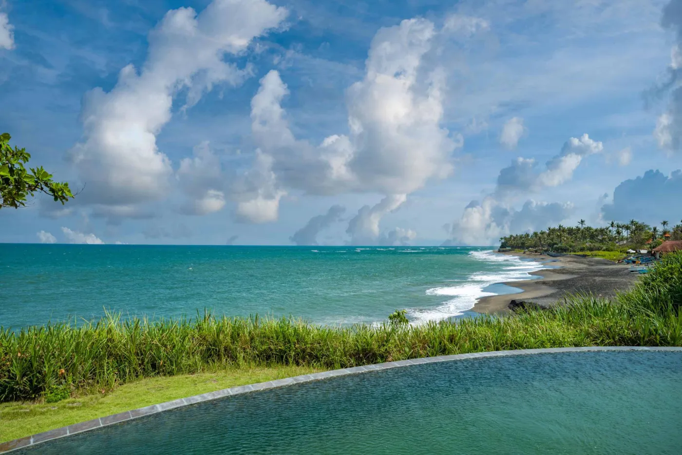 Luxurious Balinese veranda at sunset overlooking ocean and infinity pool, with wooden furniture, tropical plants, and cushioned seating. - Bali Villas