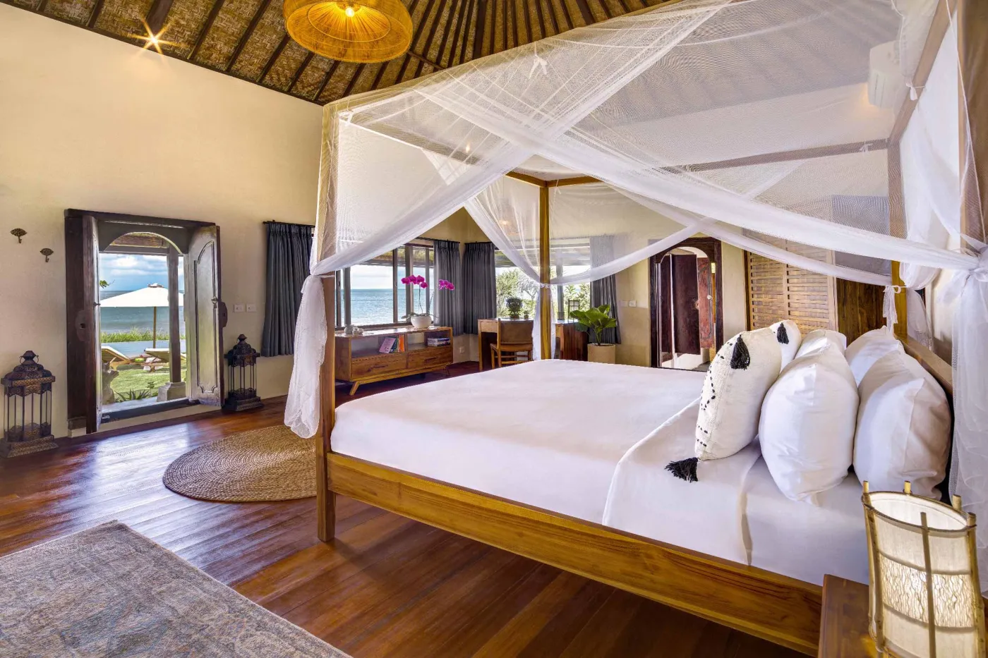 Luxurious Balinese veranda at sunset overlooking ocean and infinity pool, with wooden furniture, tropical plants, and cushioned seating. - Bali Villas