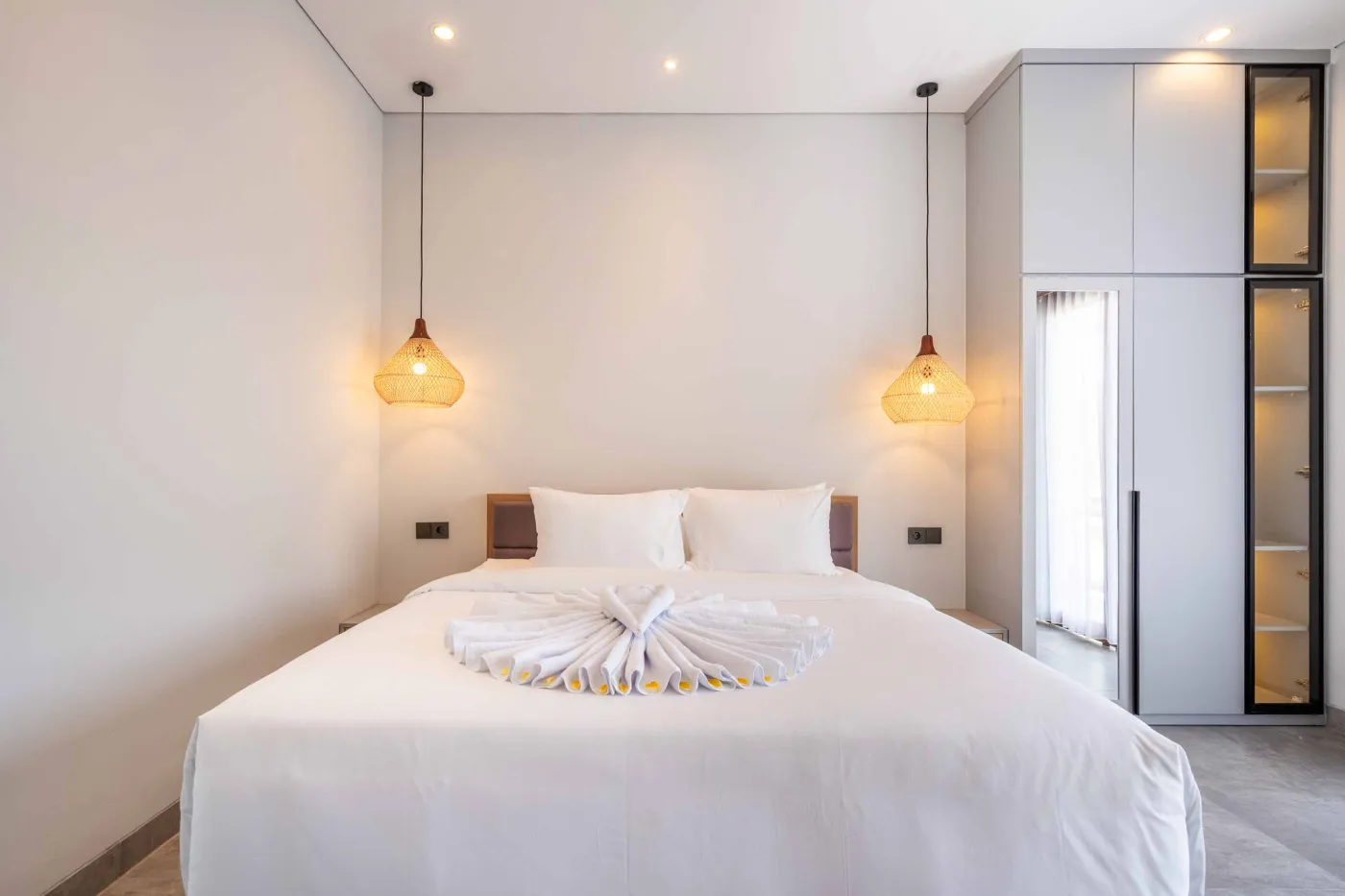 Modern Balinese-style bathroom with glass shower enclosure, round wooden mirror, stone vanity, and stacked towels. - Bali Villas