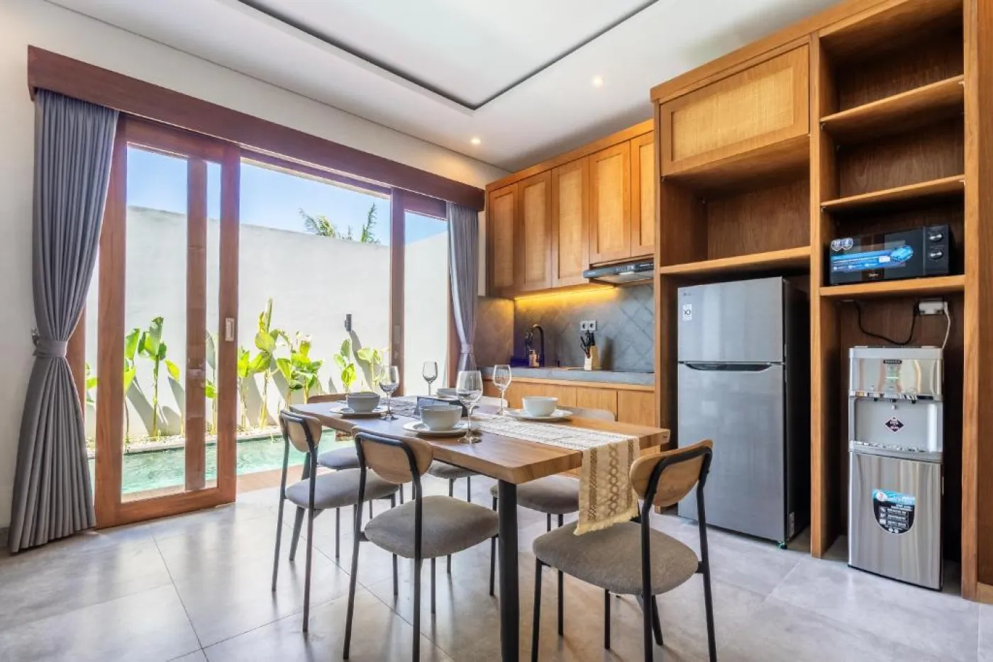 Modern Balinese-style bathroom with glass shower enclosure, round wooden mirror, stone vanity, and stacked towels. - Bali Villas